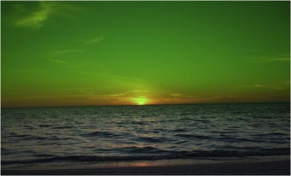 지평선 위에서 태양의 윗부분이 초록빛으로 짧게 반짝이며 나타나는 녹색섬광 현상. 주변은 붉은 일몰빛이 퍼져 있지만 태양 상단만 선명한 초록색으로 빛나는 순간.